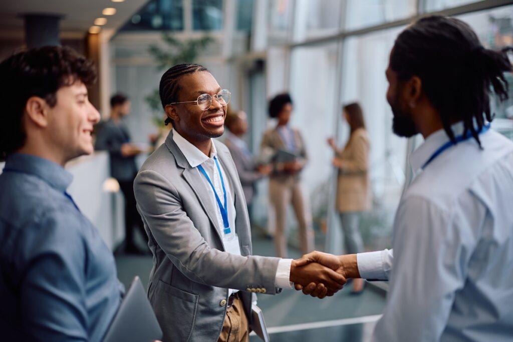 Two young professionals shake hands at a business networking event.